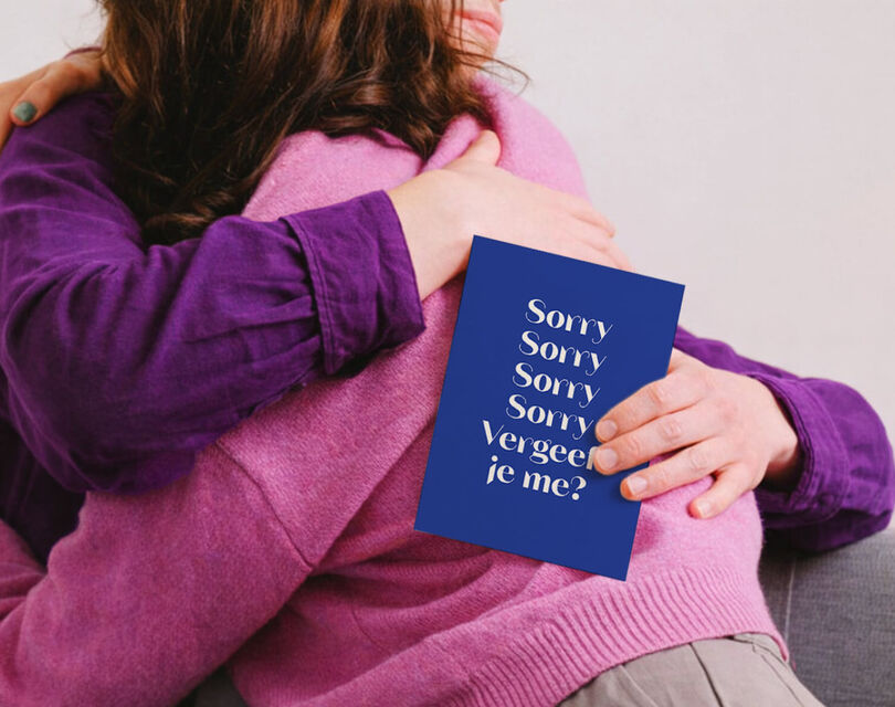 2 vrouwen knuffelen met een kaart in de hand waarop verschillende keer sorry staat
