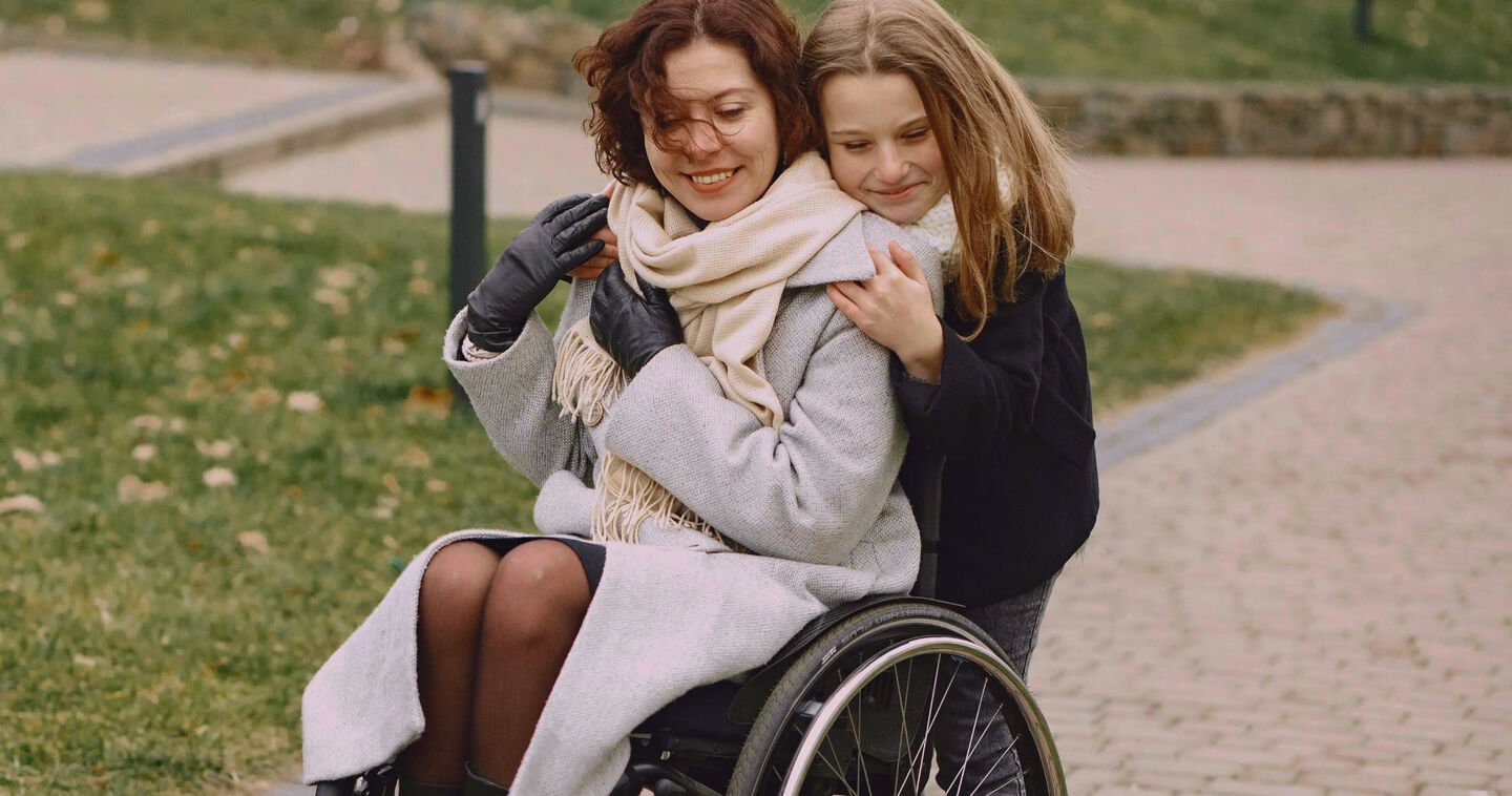 Een meisje omhelst een vrouw die een rolstoel zit