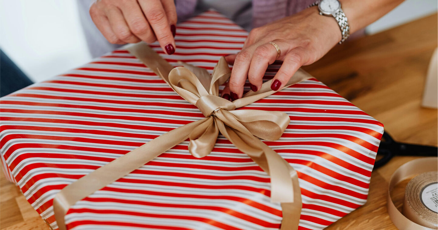 Een persoon knoopt een gouden strik rond een rood origineel ingepakt cadeau,