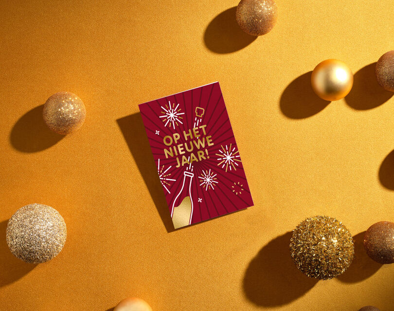 Gouden, met glitter versierde kerstballen en een rode nieuwjaarskaart tegen een goudfolie achtergrond