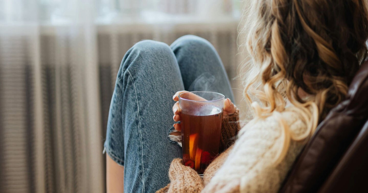 Een vrouw op de bank met een kopje thee in de hand kijkend uit het raam